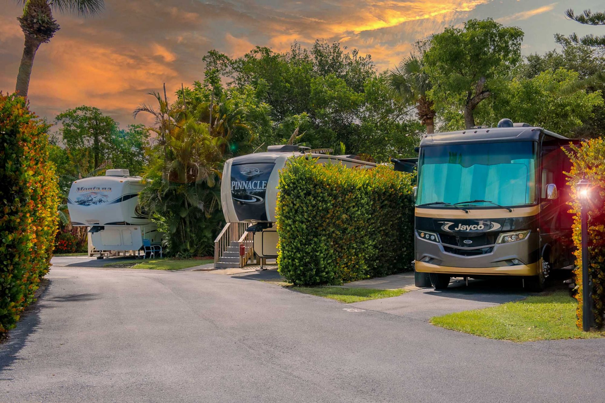 Three RVs parked in a manufactured home community next to large bushes in Naples, Florida