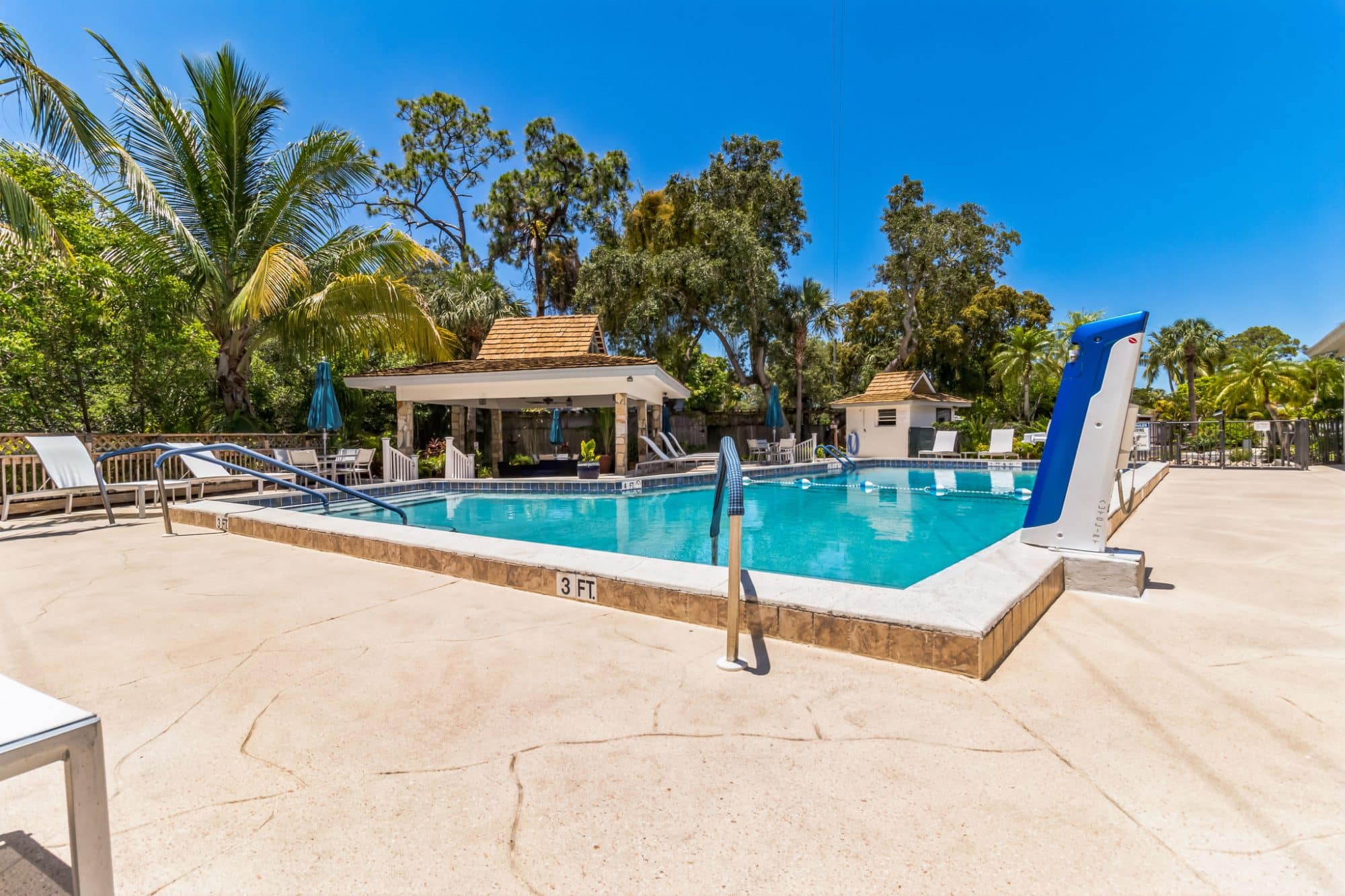 Outdoor swimming pool with a blue slide, surrounded by palm trees, lounge chairs, and a covered seating area under a sunny sky in naples fl